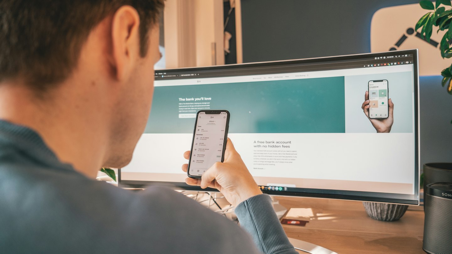 Une personne compare une application bancaire mobile à un site web sur ordinateur.